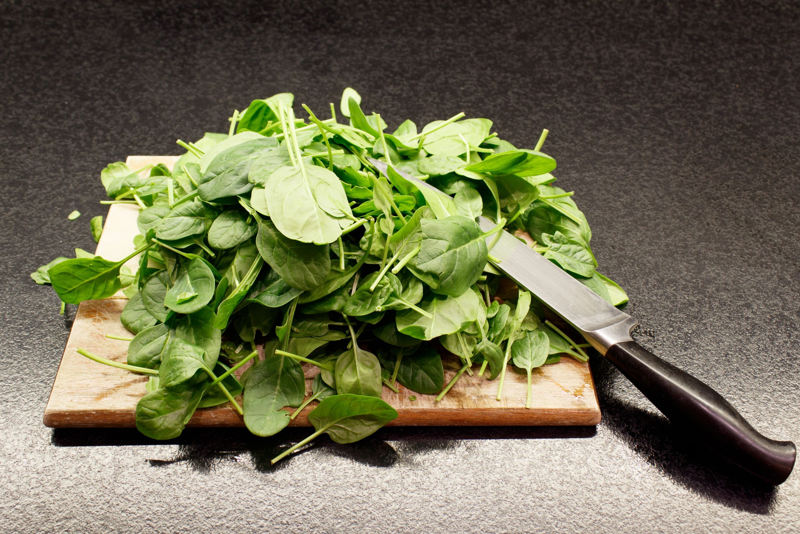 spinach on wooden cutting board, with a knife on top of it
